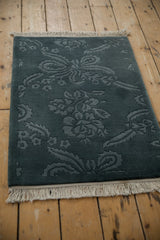 Vintage Indian rug in denim blue with a carved floral pattern and white fringe, shown from an angle.