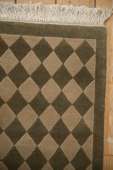 Close-up of rug fringe and corner showing carved olive green and beige checkered pattern.