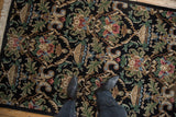 Corner of a vintage Indian Savonnerie rug with beige fringe and black ground Rococo motifs.