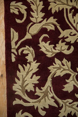 Shallow carved contour of sprawling serrated leaves in beige on a deep burgundy wool pile.