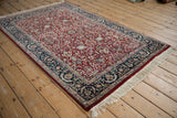 Corner of an Indian Tabriz rug showing its red vine-filled field and navy boteh border.