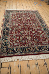 Angled view of a traditional Indian Tabriz rug with a dense red field and navy border.