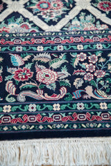 Intricate floral border in red and green on navy blue ground, adjoining the carpet's clean ivory fringe.