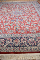 Cherry red Kashan design field with floral vinery meeting navy border, white fringe.