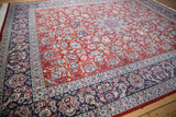 Angled view of vintage Kashan rug with cherry red field of interconnected vinery and navy border.