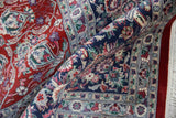 Curvilinear floral patterns in cherry red and navy on a folded vintage Kashan rug.
