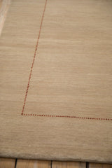 Delicate black cherry red checkered seed border on a beige contemporary Gabbeh rug.