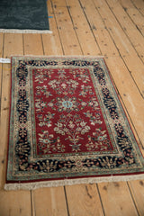 Corner of vintage Indian Sarouk rug, showing burgundy floral sprays and navy cartouche border.