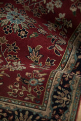 Hand-knotted pile texture, burgundy field with floral sprays, and navy cartouche border detail.