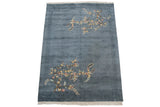 Corner of denim blue Art Deco rug with floral spray, carved border, ivory fringe.