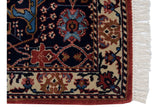 Close-up on the corner of a vintage rug showing the plush navy pile, floral palmette border, and clean fringe.