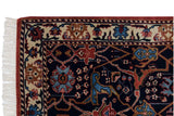 Detail of the vintage Indian rug's corner, showing the floral palmette border, brick red selvage, and clean fringe.