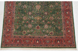 Corner of the vintage Indian Meshed rug, showing green field with palmettes, brick red floral border, and ivory fringe.
