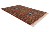 Angled view of the vintage Indian Caucasian design rug's rust field, geometric pinwheel florals, navy medallion.
