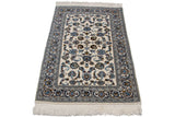 Corner of vintage Indian Isfahan rug with ivory field, navy palmettes, and white fringe.
