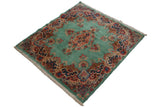 Angled view of the square vintage Kerman rug with an ocean green field, scrolling tendril medallion, and ornate floral borders.