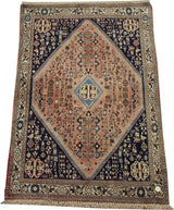 Angled view of a vintage Persian Abadeh rug with a geometric diamond medallion in navy and salmon pink.