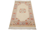 Hand-knotted Chinese Peking rug corner, displaying a mauve cartouche border with blush and seafoam florals.