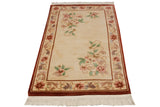 Corner of vintage Peking rug: dark cinnabar border, ivory field with soft floral vines and fringe.