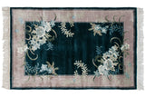 Art Deco rug corner with ivory fringe, hunter green teal field, and pale floral design relief.
