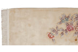 Corner of Art Deco rug, cream field, pink and mauve floral spray, and white fringe.