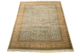Angled view of a vintage Tabriz rug with a pale blue forest scene and wide beige border.
