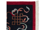Carved endless knot and cloudband motifs on a navy rug with a red border and clean white fringe.