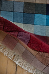 Modern Indian rug's plush pile, shallow carved contour, and graduating red and mauve blocks.