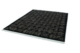 Angled view of the vintage Indian Damask carpet's black field, carved floral pattern, and white fringe.