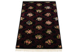 Angled view of a vintage Aubusson design carpet with floral bouquets on a black and burgundy field.