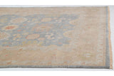 Indian Oushak carpet corner with dusty blue field, floral palmettes, sand border, and fringe.