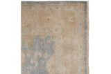 Upper right corner of Oushak design rug, dusty blue border, secured selvage, and fringe.