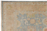 Corner of Indian Oushak carpet showing dusty blue field, wheat border, and floral palmettes.