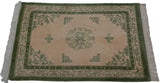 Corner view of ivory Peking rug with moss green borders, fringe, and bat motif.