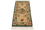 Corner of vintage Peking rug with dusty forest green border, raspberry flowers, white fringe.