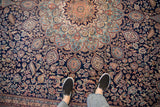 Feet on a Vintage Indian Ardebil rug, showing dense navy, blush, sky blue floral motif.