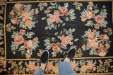 A person's view of a vintage chainstitch rug's floral pattern, showing scale and texture.