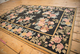 Angled view of a vintage Indian chainstitch rug with rose and gold floral bouquets on a black field.
