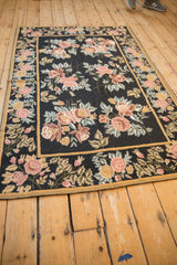 Angled perspective of a vintage floral chainstitch rug with rose and gold bouquets.