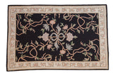 Vintage chainstitch rug with a central ribbon and sprawling floral vines in pastels on a black field.