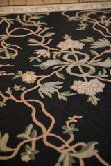 Angled detail of the intricate chainstitch weave showing a ribbon knot and sprawling floral vines.