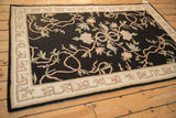 Long angle view of a vintage Indian chainstitch rug, with pastel floral vines on a black field and an ivory border.