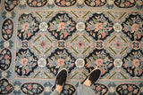 A person standing on a vintage Indian chainstitch rug with floral bouquets and a blue border.