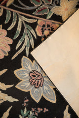A vintage chainstitch rug corner folded over, showing the floral wool weave and its canvas backing.