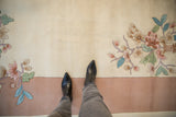 Cream Art Deco carpet with shallow carved pastel floral branches, blush border, and black boots.