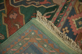 Folded corner of hand-knotted Indian Caucasian rug, showing green selvage, fringe, and geometric reverse.
