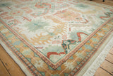 Vintage Indian Caucasian design carpet corner with ivory field, soft green and blush palmettes, intricate borders and fringe.
