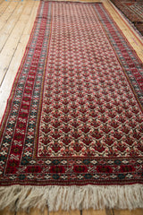 Angled view of a vintage Ardebil runner's repeating cherry red and ivory floral palmette field.
