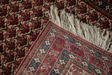 Folded corner of a vintage Ardebil rug showing the fine weave, cherry red border, and ivory fringe.