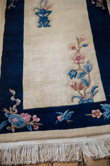 Ivory Art Deco rug corner with thick cobalt blue border, pink florals, and fringe.